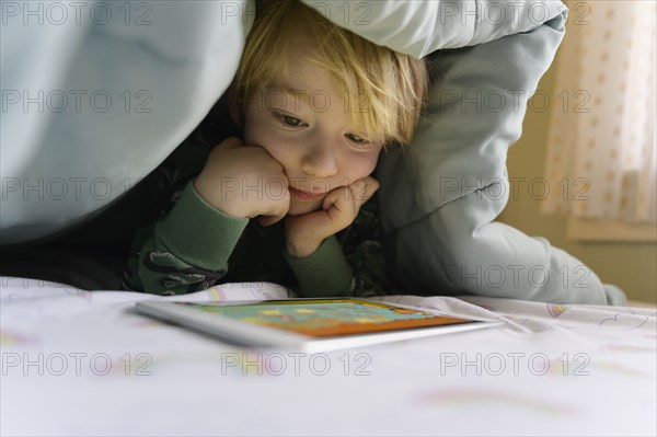 Boy (6-7) on bed looking at digital tablet