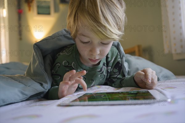 Boy (6-7) on bed using digital tablet