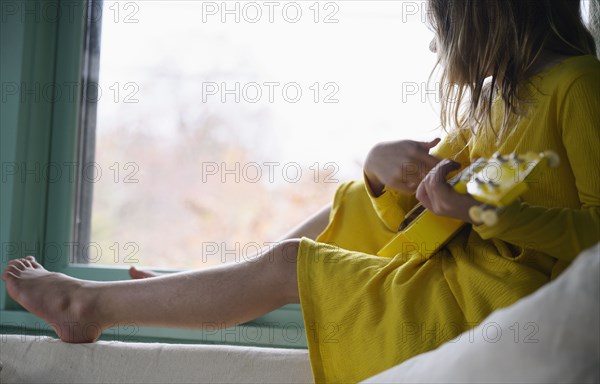 Girl (8-9) playing ukulele by window