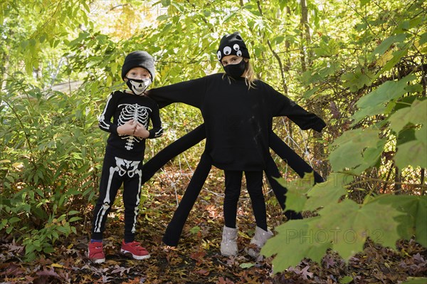 Girl (8-9) and boy (6-7) wearing Halloween costumes in forest