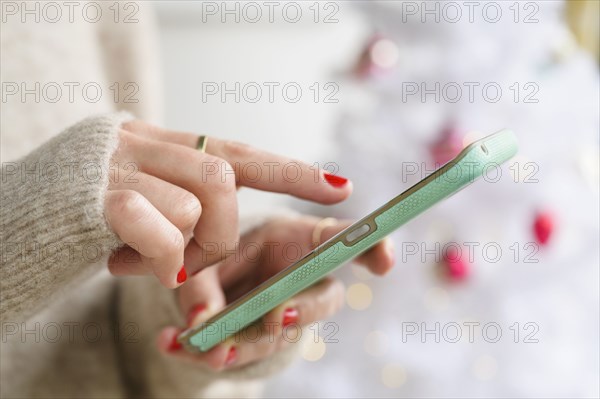 Hands holding smartphone next to Christmas tree