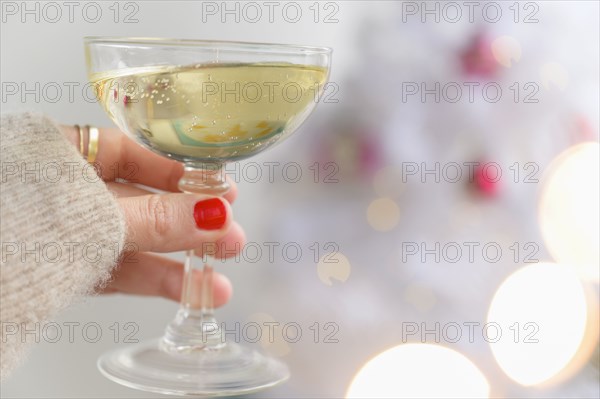 Hand holding champagne glass next to Christmas tree