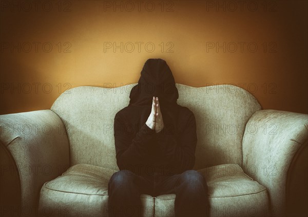 Hooded man sitting on sofa