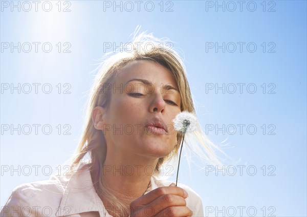 Blond woman blowing dandelion