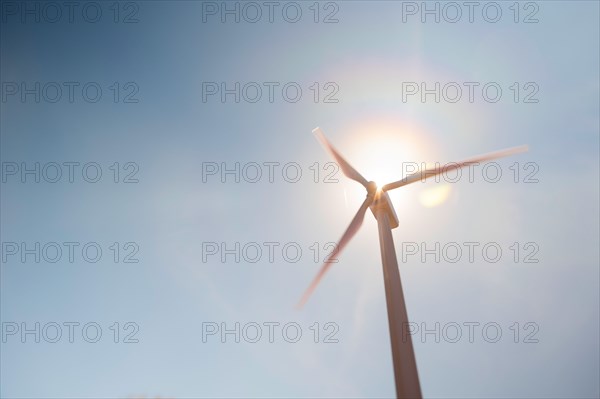 Low angle view of wind turbine against blue sky and sun