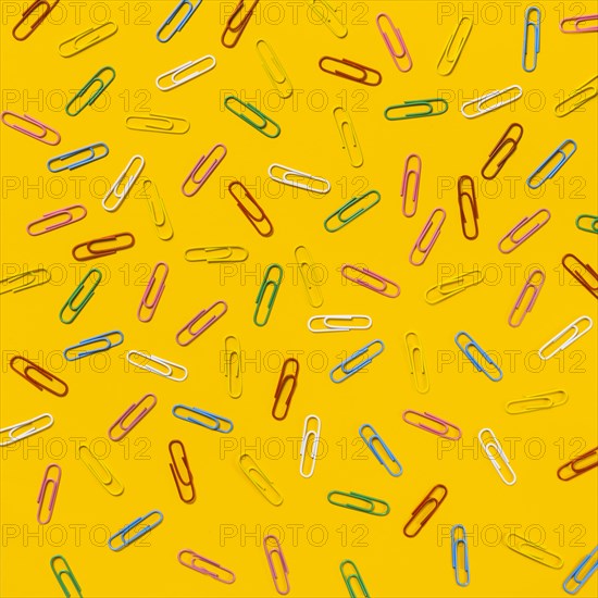 Multi colored paper clips scattered against yellow background