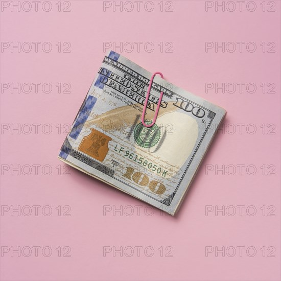 Folded one hundred dollar bill with paper clip on pink background