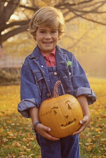 Portrait of smiling boy (4-5) holding carved Halloween pumpkin in field