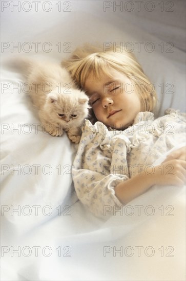 Girl (6-7) with kitten sleeping in bed