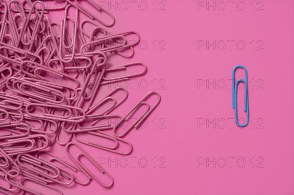 One blue paper clip and pile of pink paper clips
