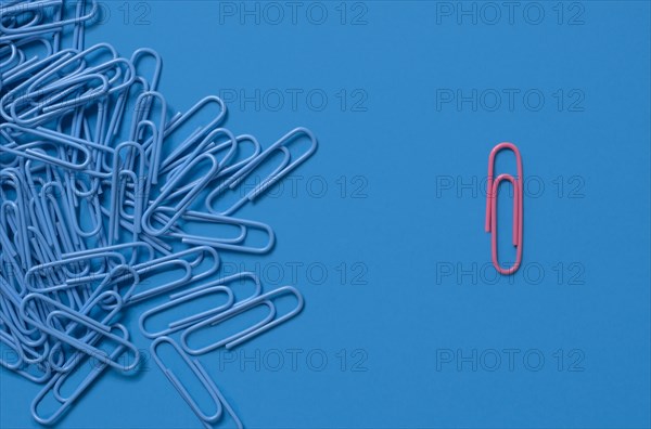 One pink paper clip and pile of blue paper clips