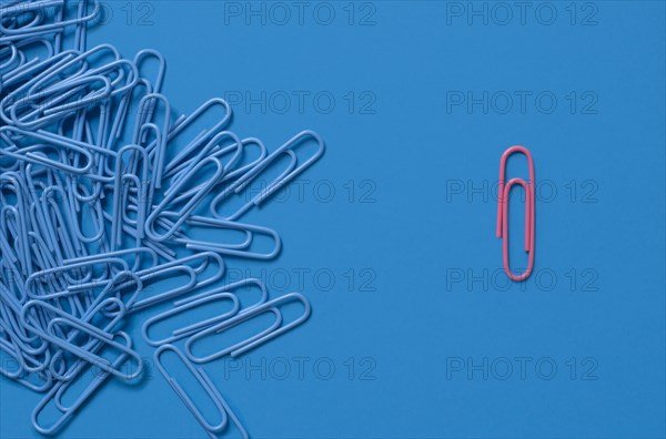 One pink paper clip and pile of blue paper clips