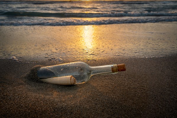 Glass bottle with message inside on beach at sunset