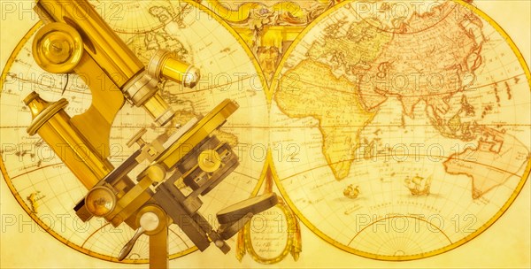 Old brass microscope against antique world map