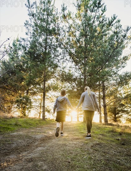 Rear view of boy and girl holding hands and walking in landscape at sunset