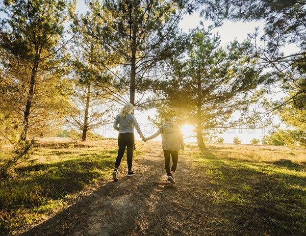 Rear view of mother and daughter holding hands and walking in landscape at sunset