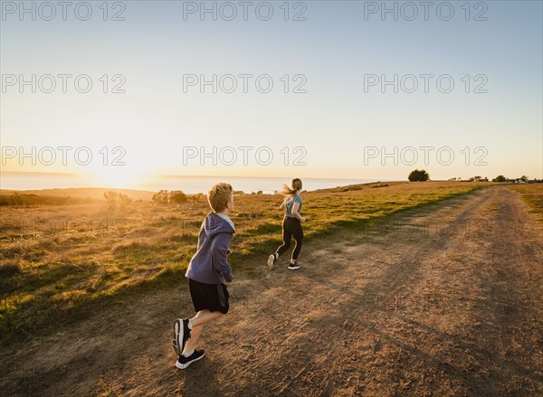 Rear view of boy and girl running on footpath in landscape at sunset