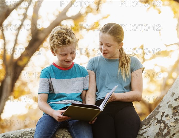 Boy and girl sitting on tree branch and reading book