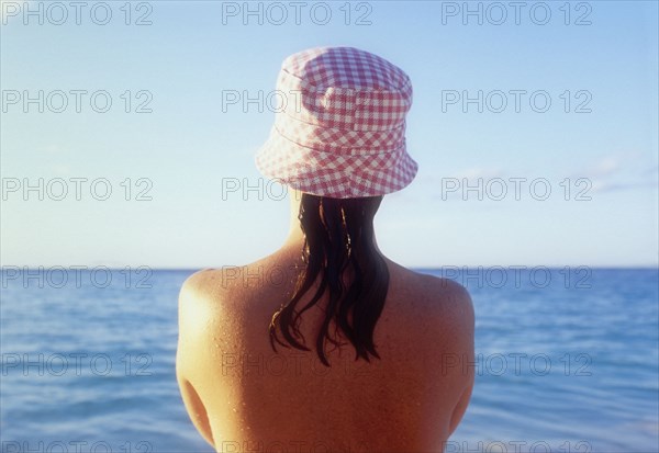 Rear view of woman in sunhat looking at sea