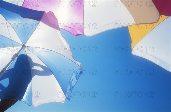 Low angle view of silhouette of woman on beach umbrella against blue sky