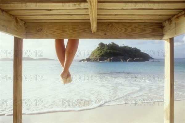Legs of woman sitting on wooden pier above sea