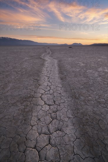 Path at cracked desert area at sunset