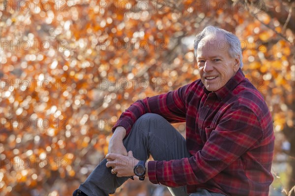 Outdoor portrait of senior man sitting near autumn tree