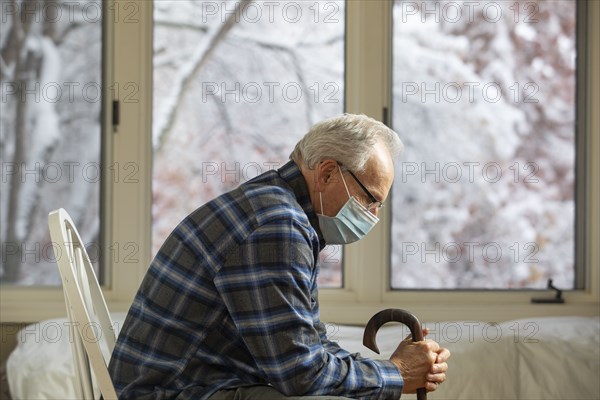 Senior man wearing protective mask sitting near window