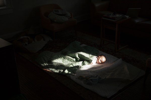 Baby boy sleeping in sunspot in bedroom