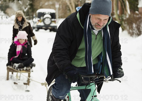 Parents and daughter playing with toboggan in snow