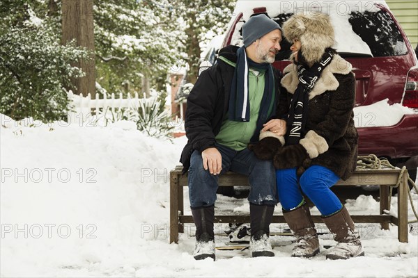 Mature couple sitting on toboggan in snow