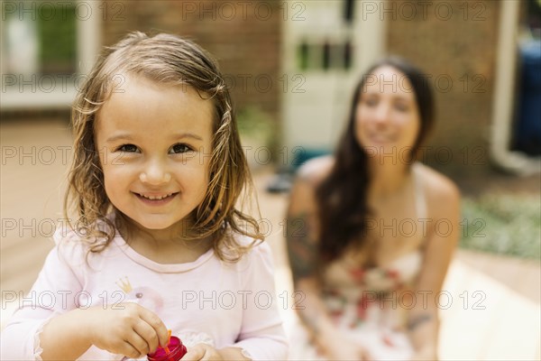 Portrait of female toddler with mother blowing bubbles in garden