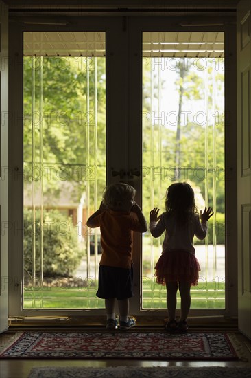 Male and female toddler friends silhouetted by patio door