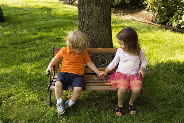 Male and female toddler friends holding hands on scaled park bench