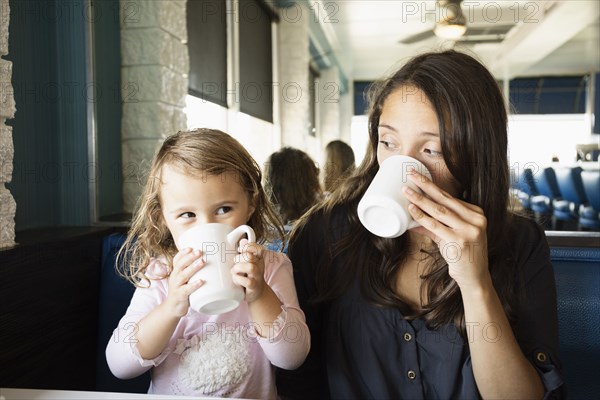 Mother and toddler drinking mugs of coffee in diner