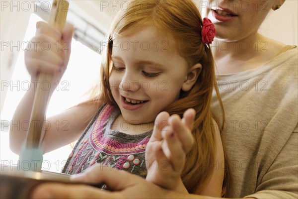 Girl mixing ingredients in bowl with mother in kitchen