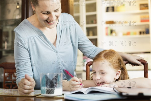 Mid adult mother helping daughter with school homework at dining room table