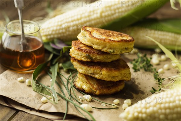 Stack of corn fritters with honey and corn cobs on kitchen table