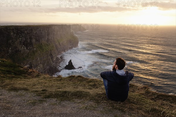 Mid adult man sitting on The Cliffs of Moher