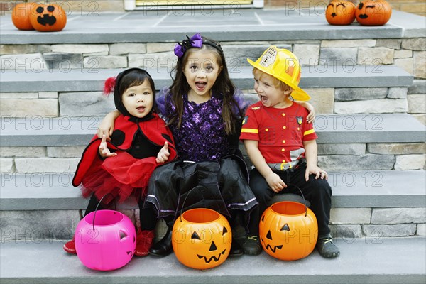 Three children sitting on steps with trick or treat buckets