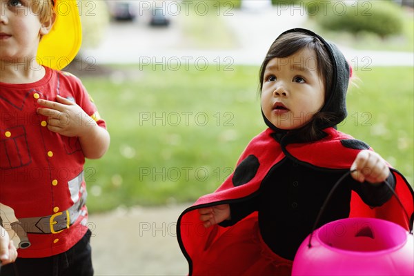 Girl and boy wearing fancy dress costumes with trick or treat bucket