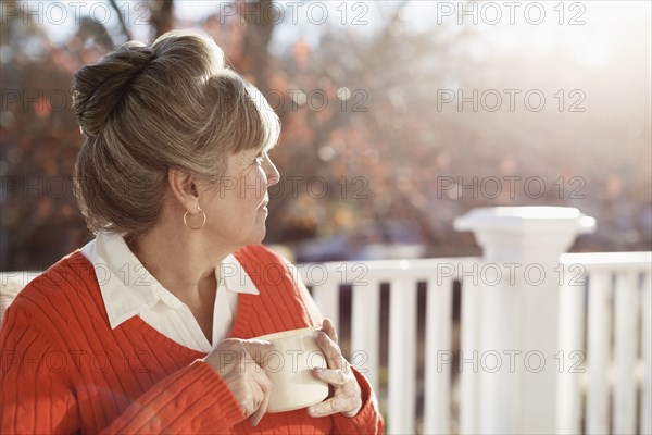 Senior woman drinking coffee and looking over shoulder from porch