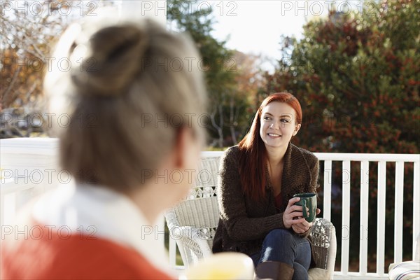 Senior woman and adult daughter chatting and drinking coffee on porch