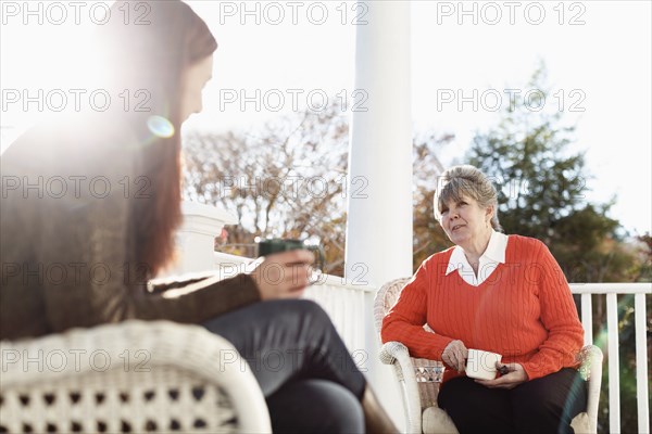 Senior woman and adult daughter drinking coffee on porch