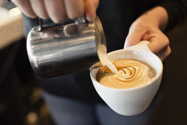 Coffee shop barista pouring milk into coffee