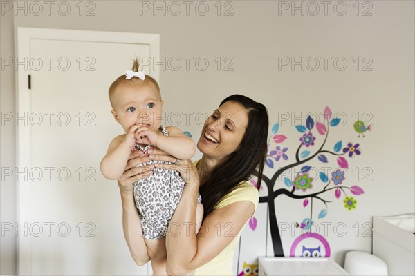Happy mid adult mother holding up baby daughter