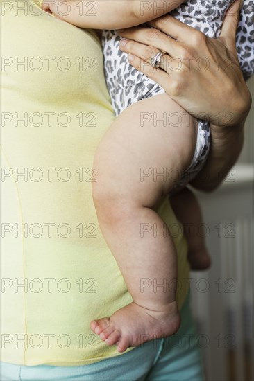 Cropped close up of mid adult mothers torso and baby daughters legs and bare feet