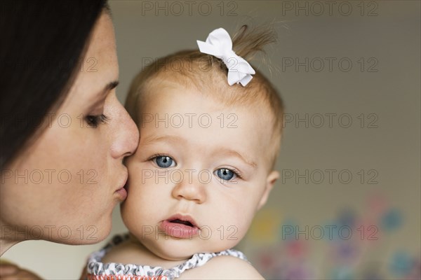 Close up of mid adult mother kissing baby daughter on cheek