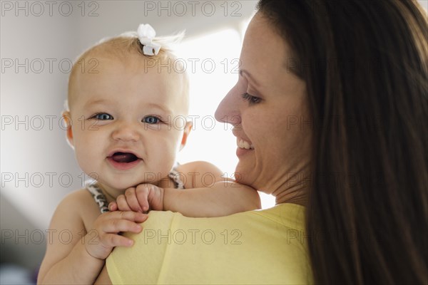 Over the shoulder portrait view of happy baby girl and mid adult mother