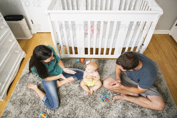 High angle view of mid adult couple playing with baby daughter on nursery rug